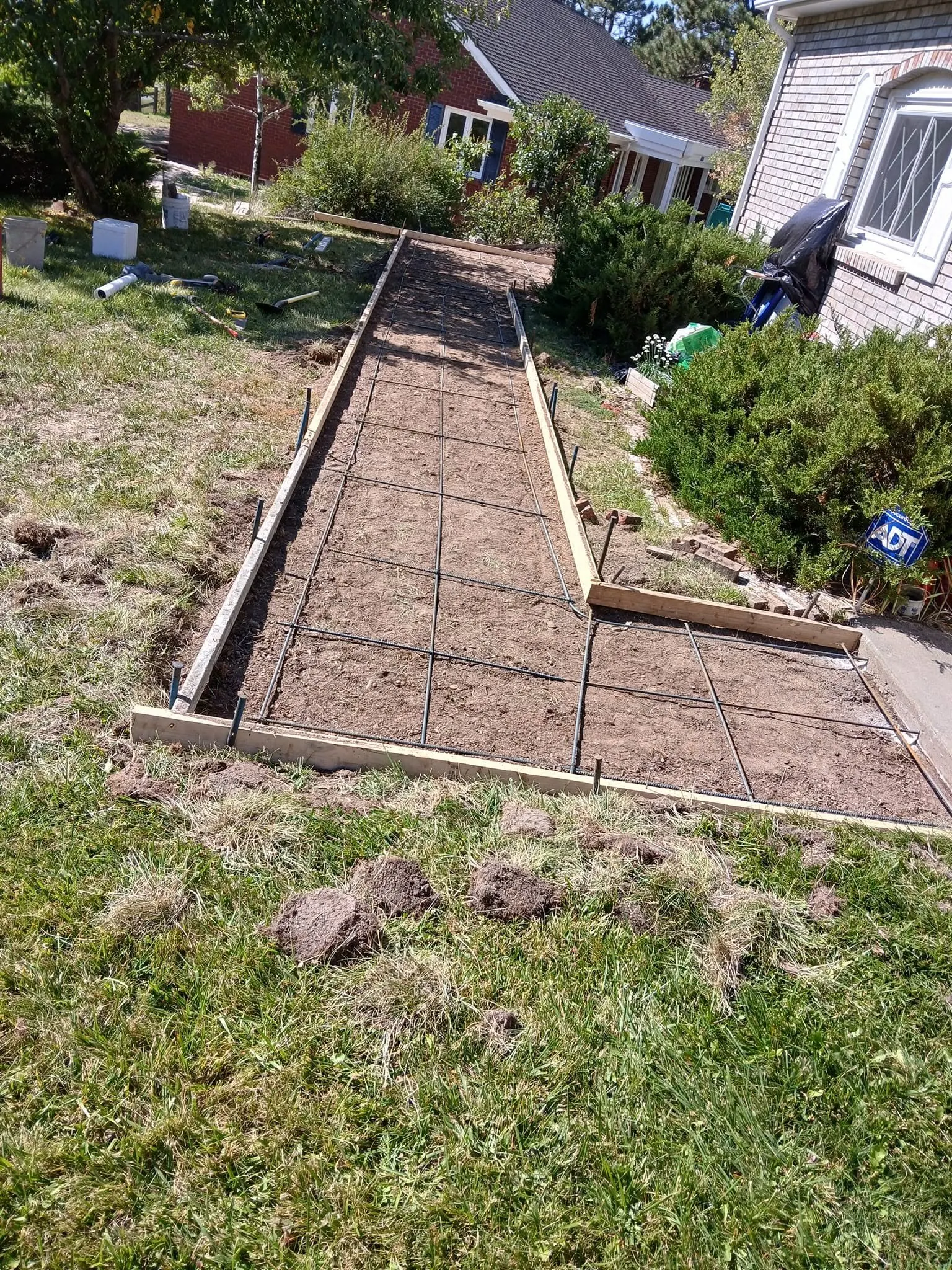 A front walkway staked out with timber forms and steel reinforcing mesh laid over graded dirt.