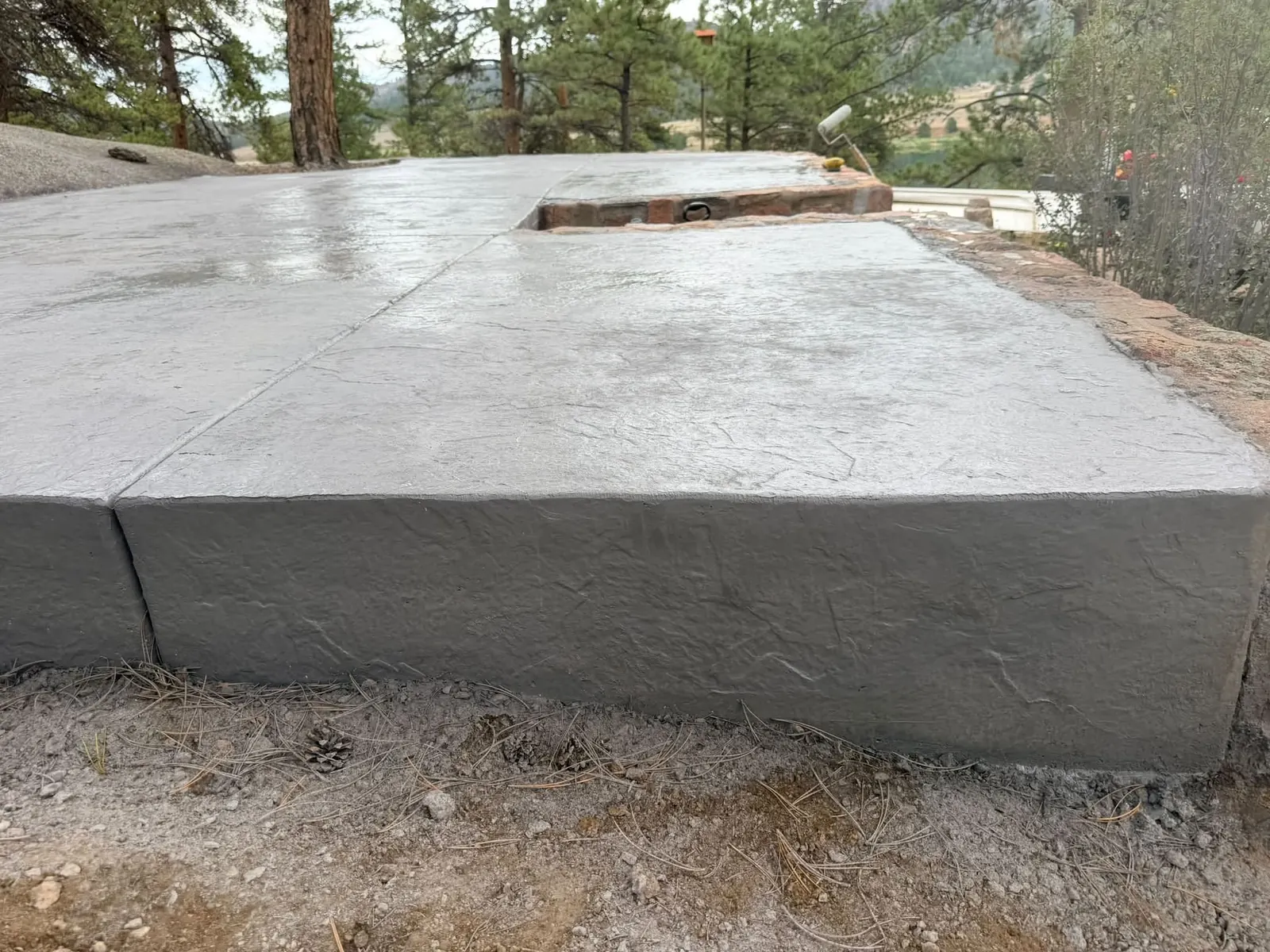 A pale seamless-slate stamped slab on a forested foothills lot with ponderosa pines and native sandstone.