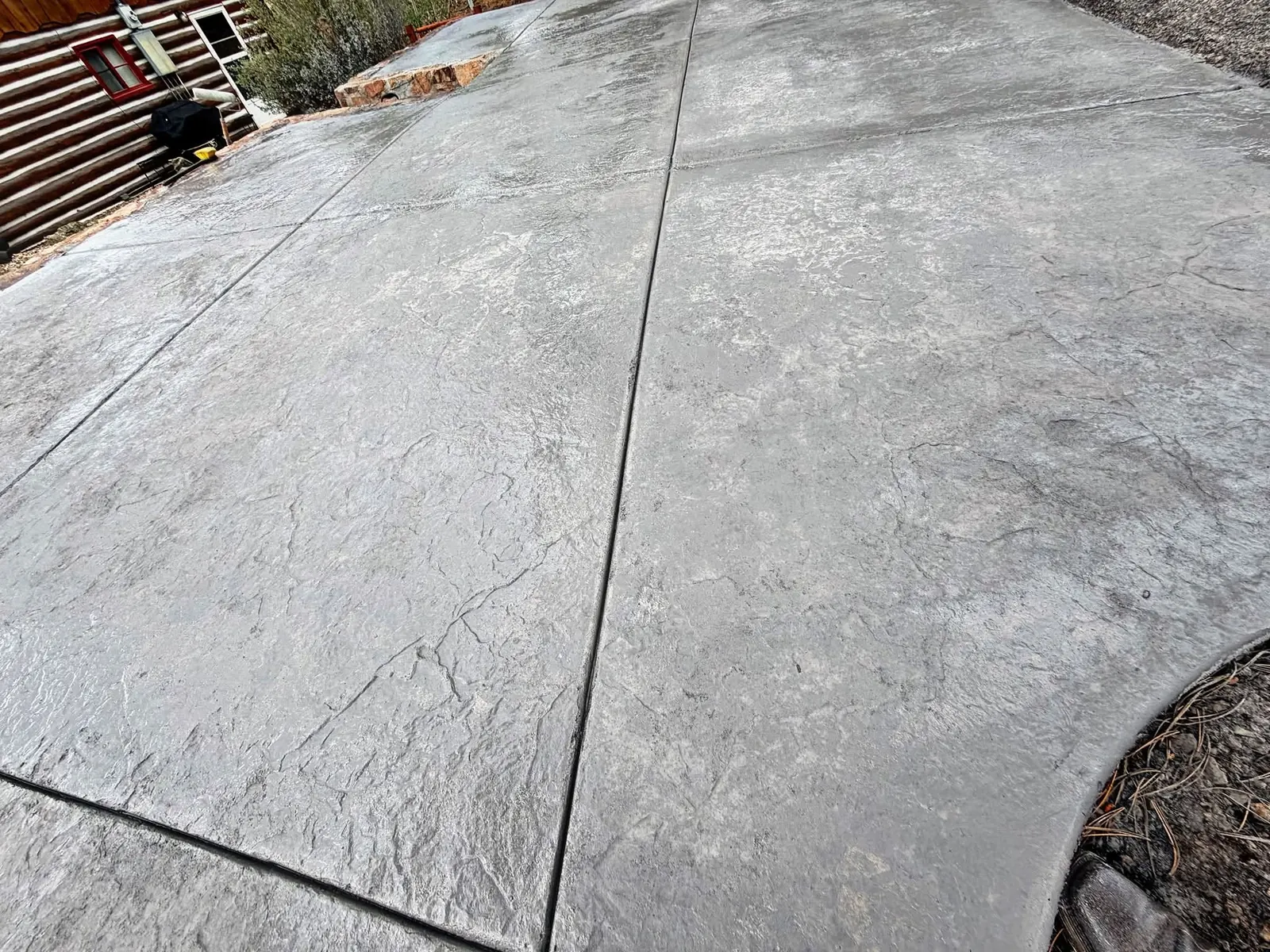 A large seamless stone-textured stamped slab beside a log home, with a curved edge following the grade.