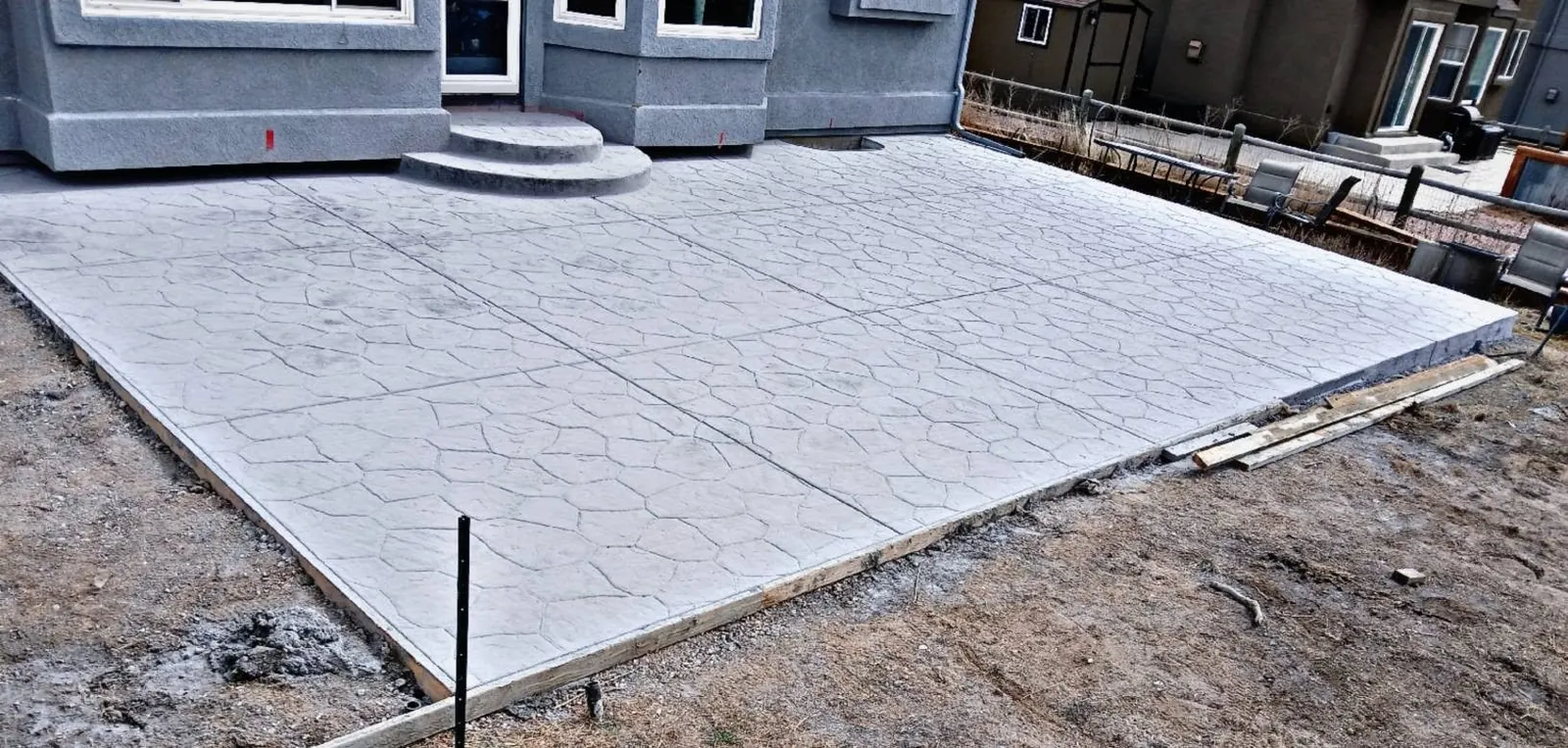 A wide pale-grey ashlar stamped patio with a rounded bullnose step at the back door of a grey stucco house.