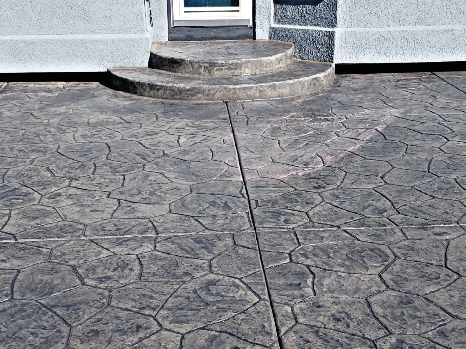 A charcoal ashlar stamped patio with two rounded bullnose steps leading to a back door.
