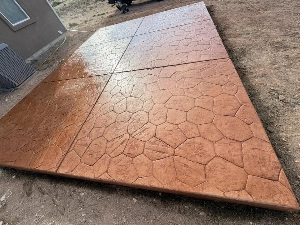 A copper-toned ashlar-pattern stamped concrete pad, freshly sealed so the colour reads deep and wet.