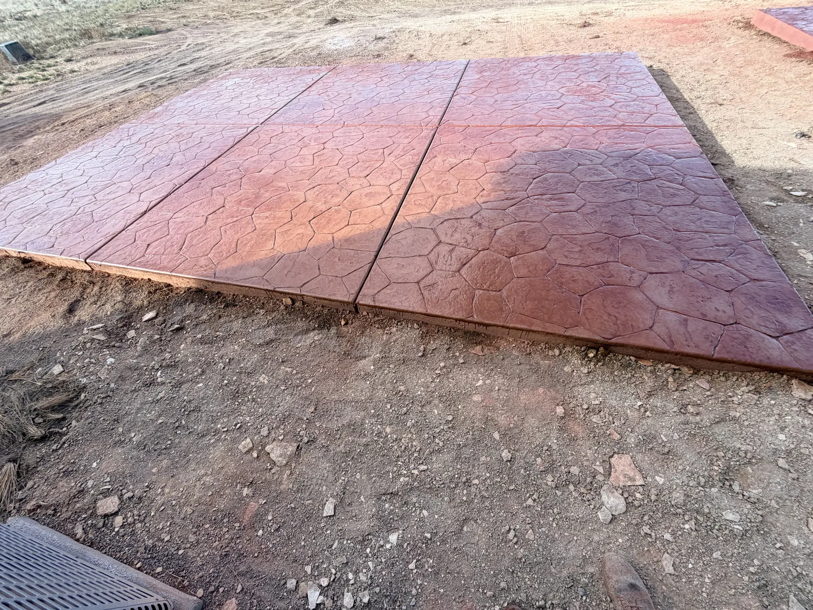 A terracotta-colored stone-pattern stamped concrete slab, cut into panels, on freshly graded ground.